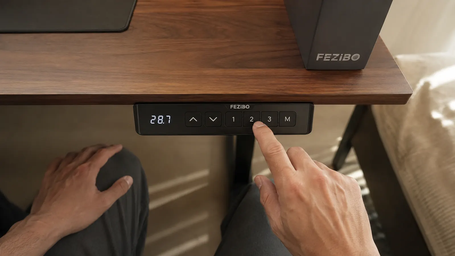Hand pressing a memory preset button on the FEZIBO desk's control panel mounted under the desktop edge