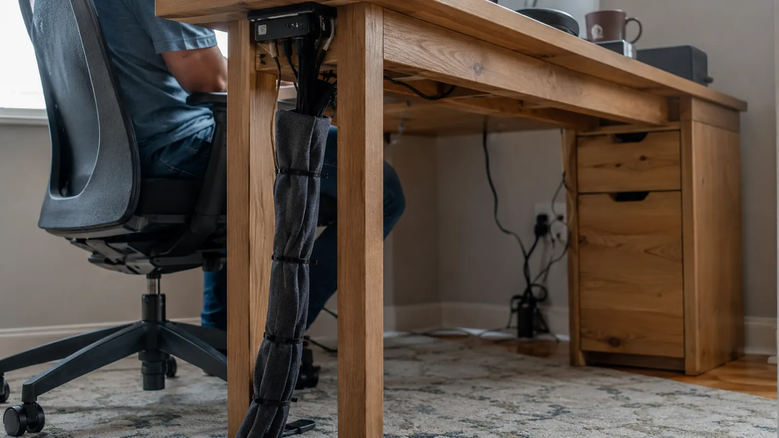 Underside view of the standing desk showing cables gathered into a sleeve and routed along one leg