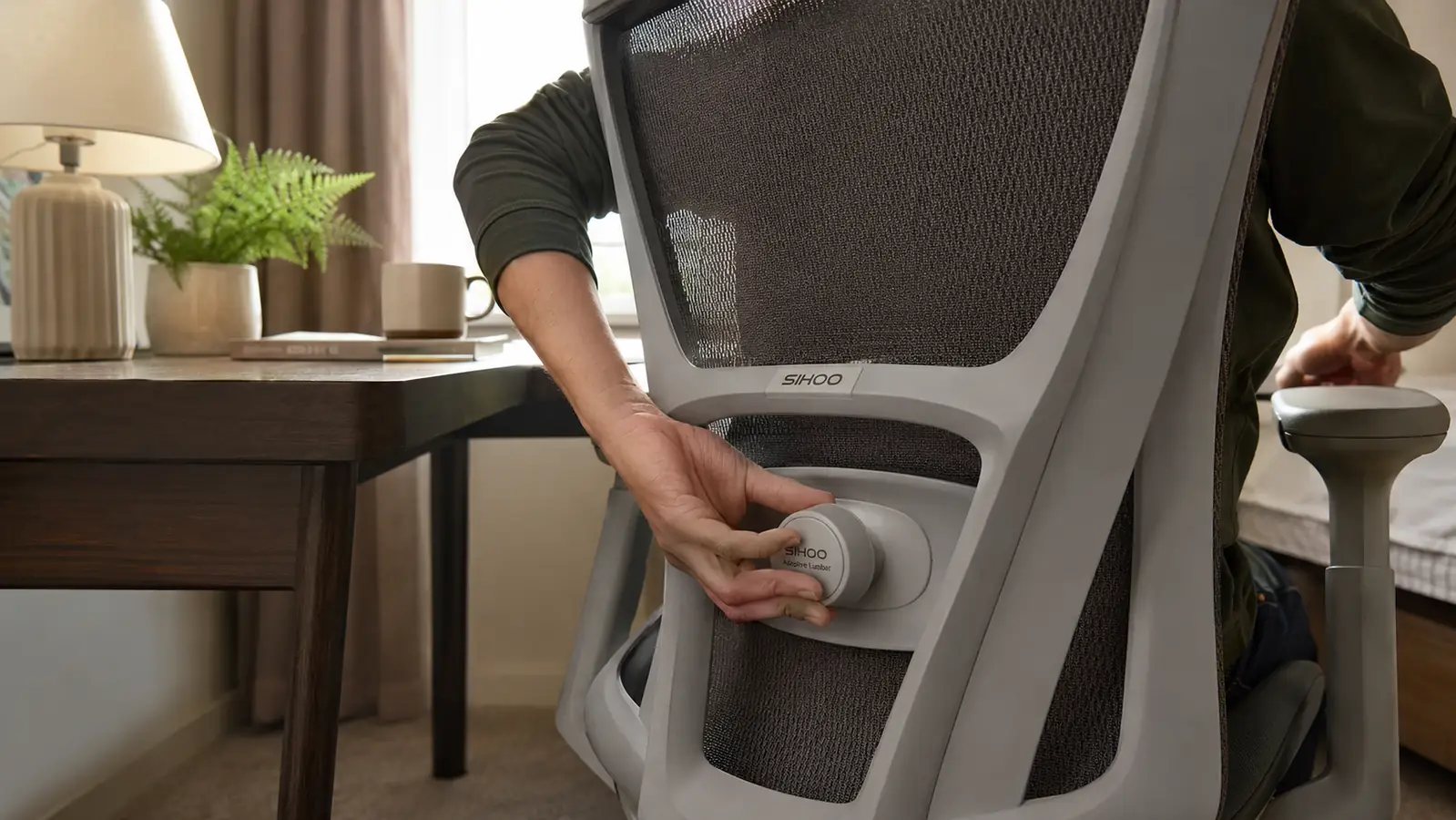 Close-up of hand adjusting the lumbar support dial on the back of a mesh office chair