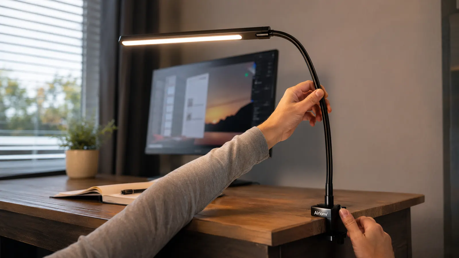 A hand adjusting the gooseneck arm of the Airlonv desk lamp clamped to the edge of a desk