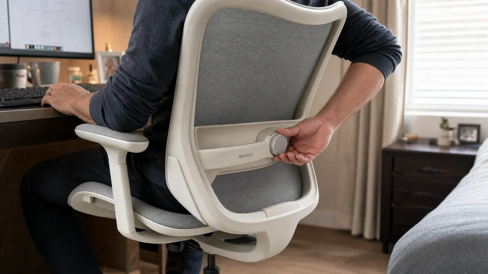 Close-up of hands adjusting the lumbar support dial on the back of a mesh office chair