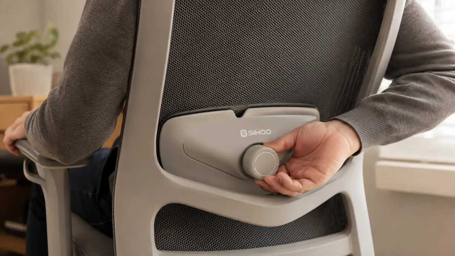 Hand adjusting the lumbar support dial on the back of the SIHOO B100 chair
