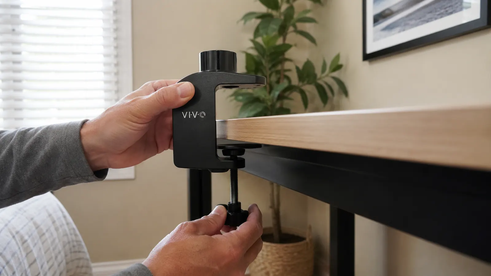 Hand test-fitting the VIVO C-clamp against the back edge of a desk before tightening it down