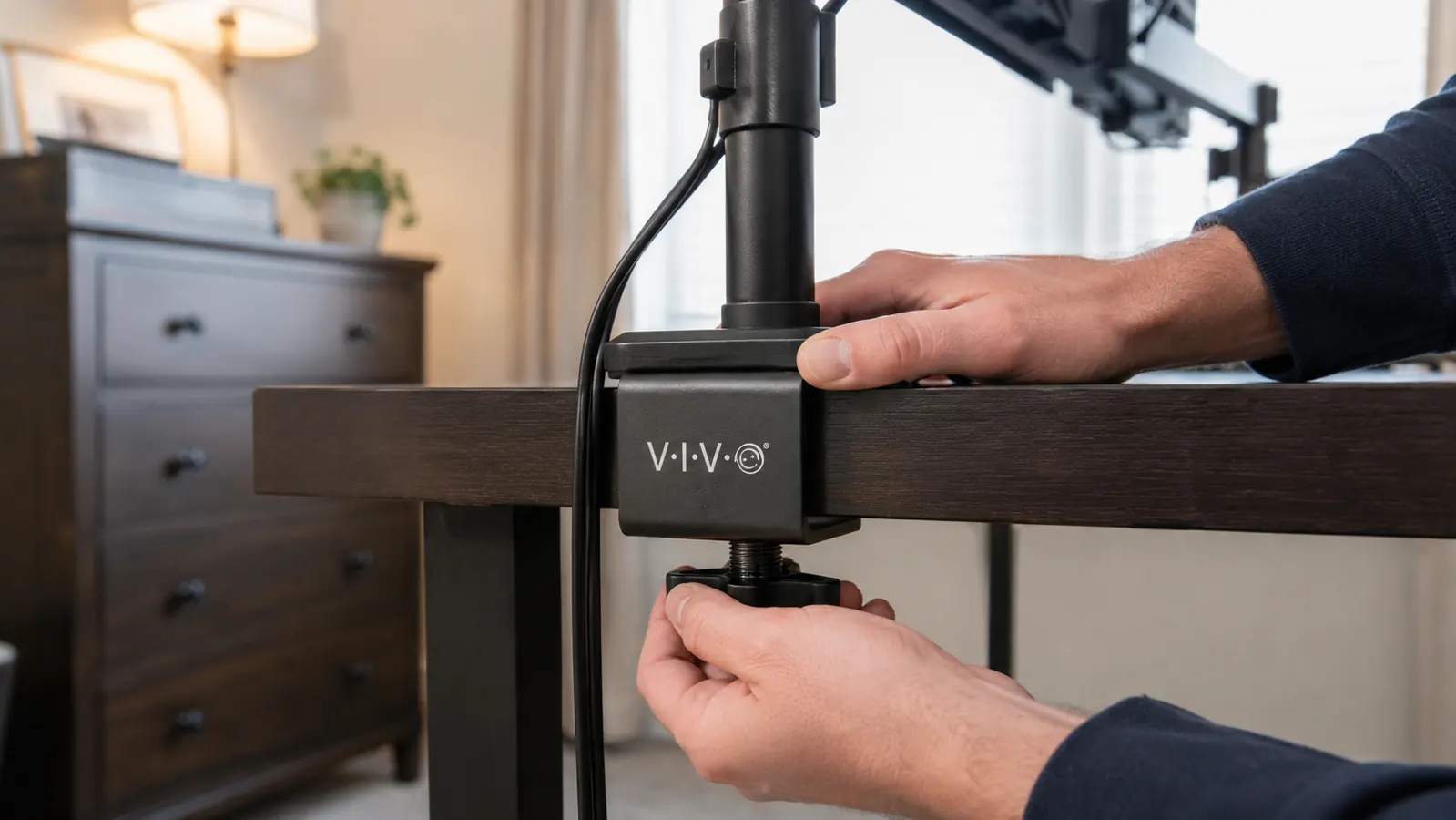 Hand tightening the C-clamp of the VIVO dual monitor desk mount onto the back edge of a desk